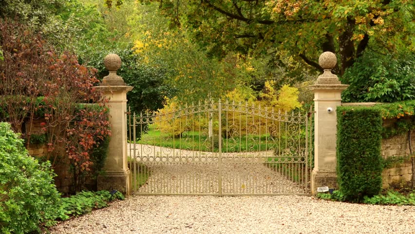 Ornate wrought iron gate opening to a beautiful garden at an English country estate in autumn. Cotswolds countryside, England
