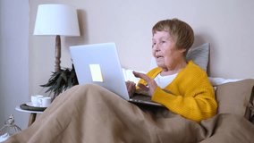 Happy senior woman communicating with family through a video call on her laptop while sitting comfortably in bed, staying connected with modern technology and enjoying her retirement at home - Powered by Shutterstock - Get 15% off with code: PIKWIZARD15
