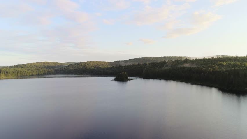 Reverse Aerial Rise to Reveal Golden Hour Lake. A fast, accelerated drone shot flies backward over treetops and islands, rising high to reveal the entire pristine lake at sunrise.