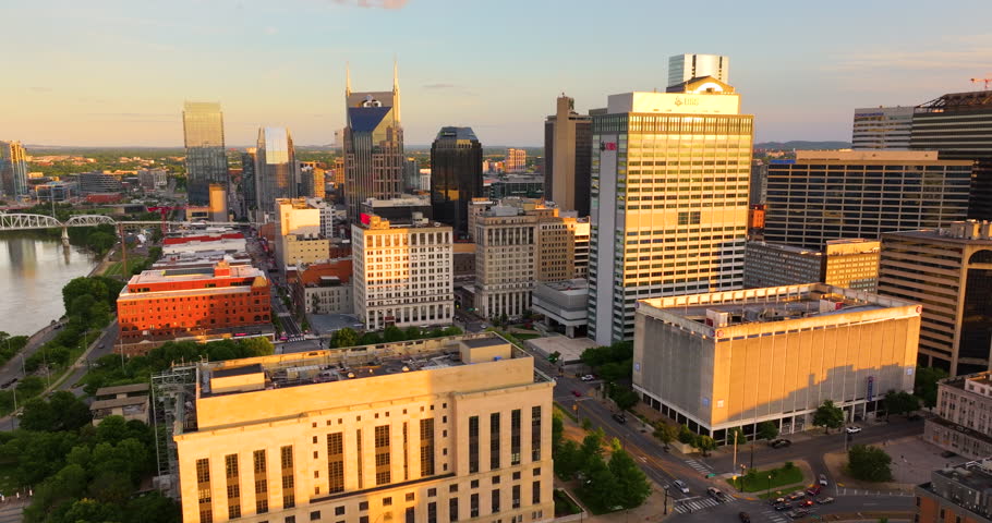 Drone shot of Nashville, Tennessee with urban layout, high buildings and city blocks below illuminated with warm evening sun.
