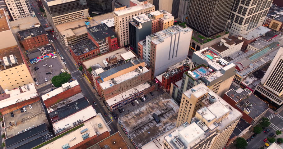 Drone shot of Nashville, Tennessee with urban layout, high buildings and city blocks below illuminated with warm evening sun.
