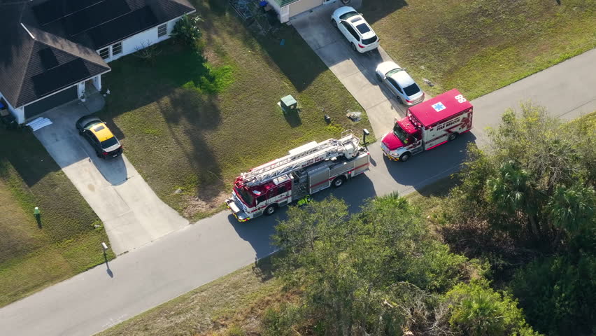 Medical personnel treat resident at home as emergency vehicles block quiet suburban street.