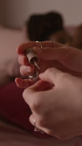 Vertical close-up of hands of anonymous fair-skinned girl painting nails with clear nail polish or growth serum, while trying out new grooming routines at slumber party with friends