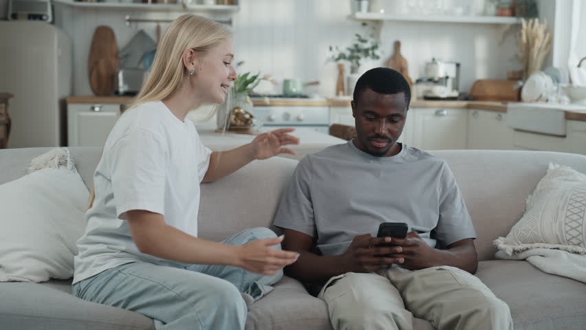 Social media addicted man does not hear scream of his wife, smartphone overuse. Multiethnic married couple, troubled relationship and misunderstanding, interracial lovers, mobile gadget addiction