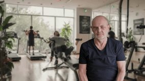 A senior man trains in a modern gym, gripping weighted dumbbells with intensity. Background shows others on treadmills, plants, and bright natural light creating an energetic fitness scene. - Powered by Shutterstock - Get 15% off with code: PIKWIZARD15