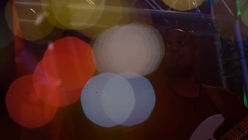 Colored bokeh circles drifting reveal bassist plucking strings on green-lit stage to showcase music. Concert, musician, illumination, performance, artistry, ambiance, entertainment