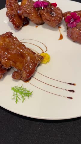 An artistically plated sweet and sour short ribs with flowers and balsamic glaze.