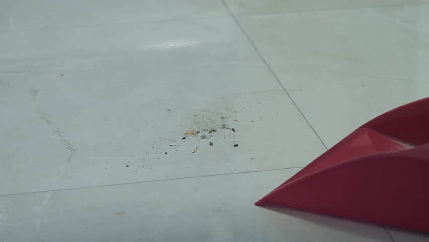 Close-up view of floor cleaning with broom and dustpan in apartment kitchen. Domestic atmosphere, everyday home routine. Person doing chores