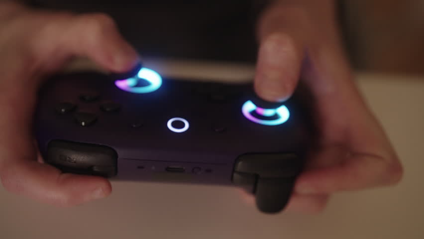 Close-up of unrecognizable woman with cerebral palsy holding gaming controller, hands illuminated by bright blue and white lights of device, finding enjoyment, independent leisure activities at home