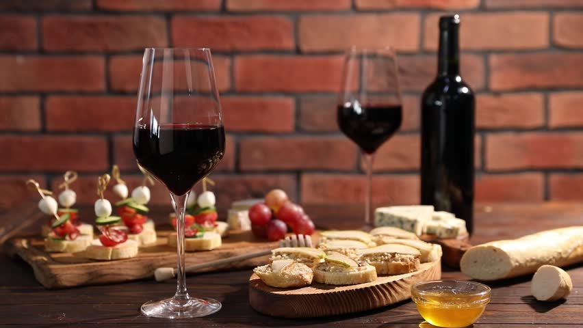 Woman taking glass of red wine at wooden table with tasty bruschettas against brick wall, closeup