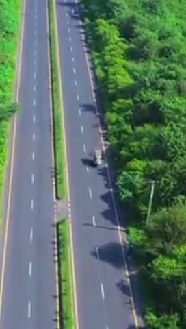 Aerial drone footage showing a beautiful double road surrounded by lush green trees on both sides.