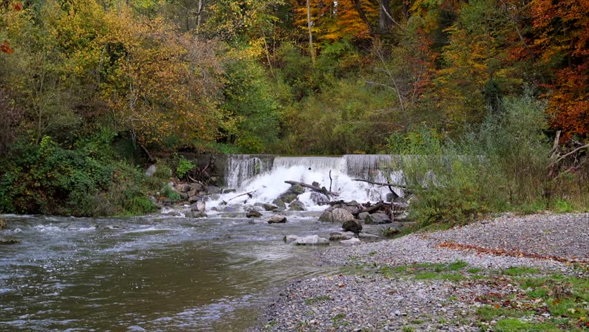 Beautiful small waterfall in an autumn forest. Scenic natural landscape with flowing water, mossy rocks, and colorful foliage. Peaceful nature scenery capturing the beauty of the fall season