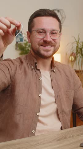 Young businessman real estate agent lifting hand showing the keys of new home house apartment, buying renting property, mortgage loan at office workplace. Happy freelancer broker man using laptop.