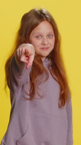 Hey you. Happy young child girl kid smiling excitedly and pointing forward to camera, choosing lucky game winner, indicating to awesome you, promotion. Teenager children isolated on yellow background