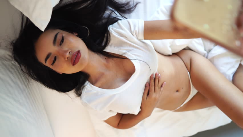 Sexy Asian Woman Posing For Selfie Smartphone Camera, Lying in Bed in White Lingerie, Slow Motion
