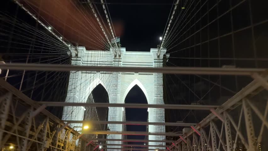 View from car window of the lights of the Brooklyn Bridge shining at night while driving under the arches
