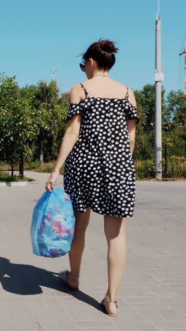 Back view, girl is carrying a package of garbage in her hands, throwing out trash. summer hot day. ecology. separation of debris, cleanliness of the environment