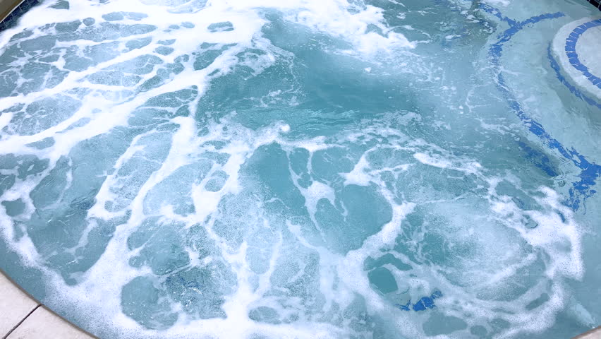 A close view shows bubbling water cascading over tiled hot tub steps. The steps are trimmed in blue tile, and the motion of water is clearly visible.