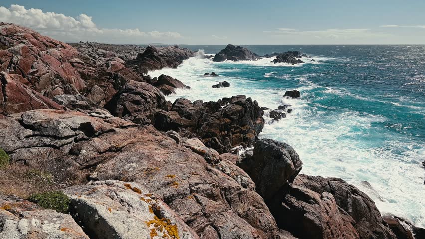 Strong atlantic ocean waves crashing against the rugged granite cliffs of the spanish coastline on a sunny day, showcasing the raw power of nature and the beauty of the seaside landscape
