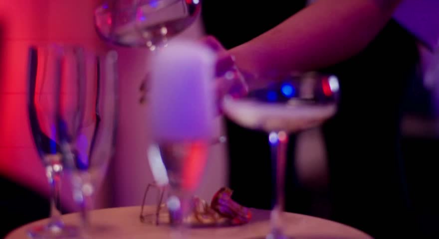 A close-up shot captures the effervescent pour of champagne into an elegant coupe glass, set against a vibrant, blurred background of red and purple lights, evoking a festive and celebratory atmospher
