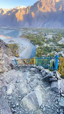 An epic high angle view of the Indus River winding through a lush green valley framed by sunlit snow capped mountains at sunset
