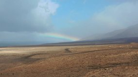 Natural landscape in Fuerteventura, Canary Islands  a dirt path through arid land facing the sea, with a colorful rainbow breaking through dramatic clouds. - Powered by Shutterstock - Get 15% off with code: PIKWIZARD15