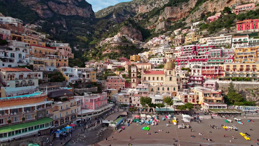 Scenic coastal town with colorful houses along blue water and green cliffs.