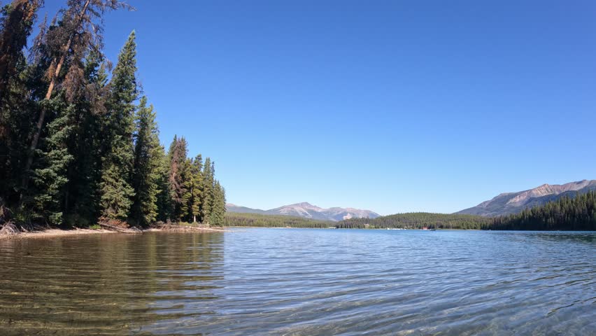 Canoe boating on a large mountain lake with small waves reflecting evergreen trees, blue sky and distant mountains