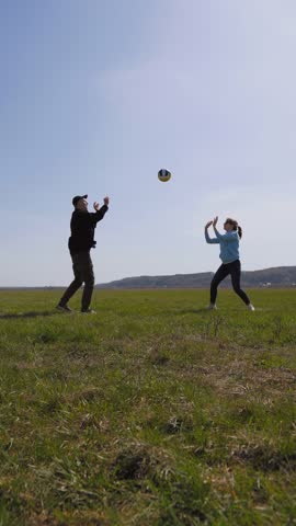 Joyful young couple having fun and playing volleyball together on a green grassy field on a sunny day, enjoying an active outdoor lifestyle and spending quality time with each other vertical video