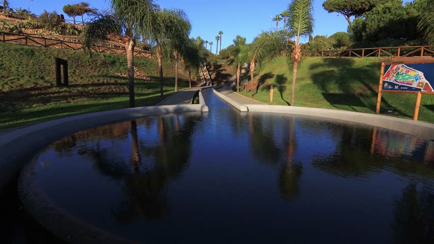 Peaceful path with palm trees and pond at sunset in José Celestino Mutis Botanical Park, Palos de la Frontera, Huelva, Spain. Nature and travel concept.