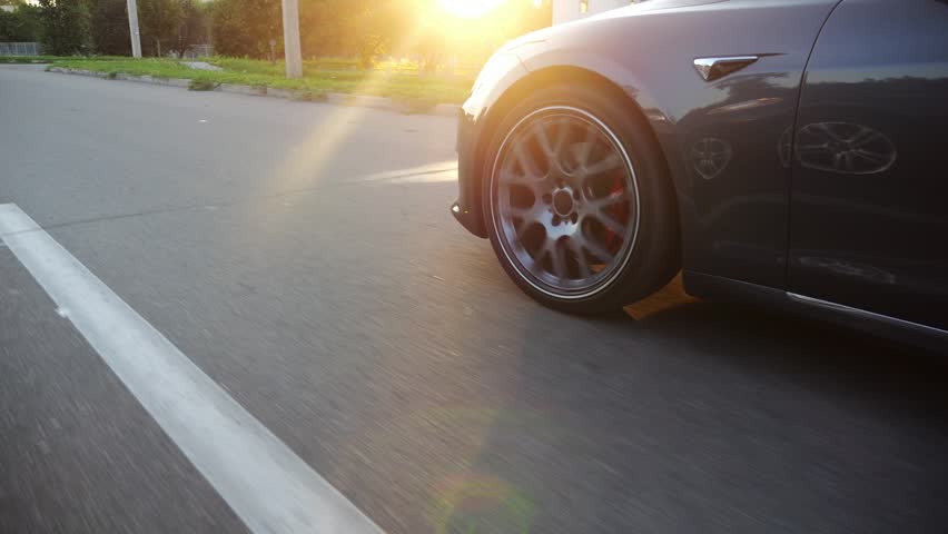 Wheel of modern electrical automobile driving at urban road on sunny day. Ecology friendly car riding moving along motorway. Electric vehicle riding through empty highway. Green innovation concept