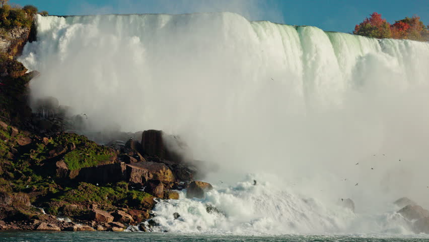 Powerful waterfall crashing over rocky cliffs with mist rising into the air on a sunny day at Niagara Falls. High quality 4k footage