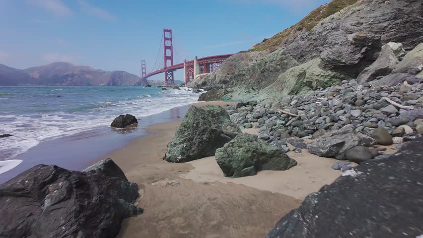 Waves roll onto sandy shore at Baker Beach with Golden Gate Bridge in background, San Francisco, California, USA. Iconic coastal view with ocean, rocks and Marin Headlands