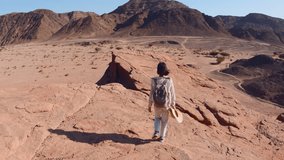 A woman with a backpack walking in the desert. Trekking and hiking in the desert. Back view. Timna National Park. Israel. Tourist in the desert. - Powered by Shutterstock - Get 15% off with code: PIKWIZARD15