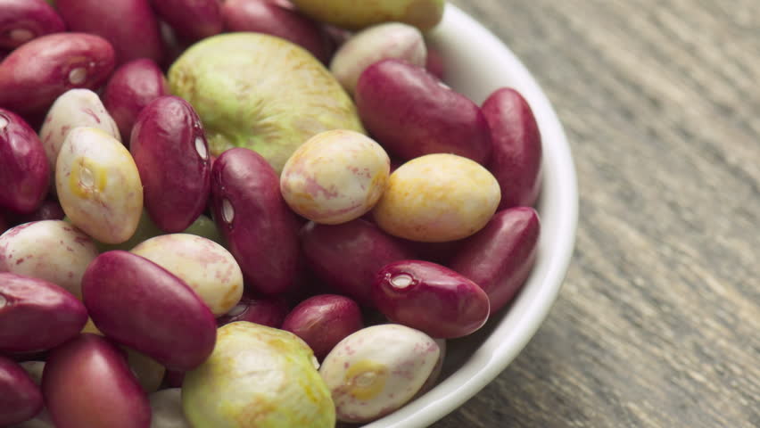 Fresh beans of different varieties and sizes on white plate. Macro shot. Colorful beans on wooden table. Product of organic farming. Healthy eco vegetarian food.