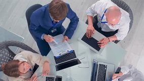 overhead client pitch around glass table, advisor presenting funding proposal to entrepreneur and senior consultant, team reviewing charts and metrics on laptop, hopeful collaborative energy in modern - Powered by Shutterstock - Get 15% off with code: PIKWIZARD15