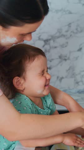 baby grins as mom cleans face, playful toddler laughs happily as mother carefully applies soap in cozy