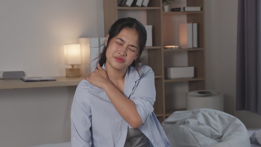 Asian Female waking up bedroom rubbing eyes and stretching after sleep young woman shoulder pain rubbing neck and shoulder bedroom night expressing discomfort young woman holding neck pain with