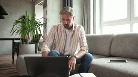 Young businessman sitting on sofa at home working on a laptop and writing notes down on a notepad - Powered by Shutterstock - Get 15% off with code: PIKWIZARD15