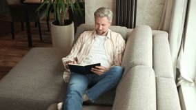 Young businessman sitting on sofa at home and writing notes down on a notepad - Powered by Shutterstock - Get 15% off with code: PIKWIZARD15