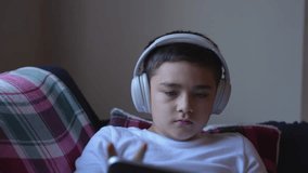 Teen boy wearing headphones and using tablet at home for online learning, entertainment, or e-books. Modern digital lifestyle of children in relaxed and tech-friendly environment. - Powered by Shutterstock - Get 15% off with code: PIKWIZARD15