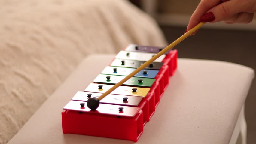 A wooden mallet glides gently across a colorful xylophone, producing harmonious sounds. The calm indoor atmosphere enhances the relaxing experience of the music