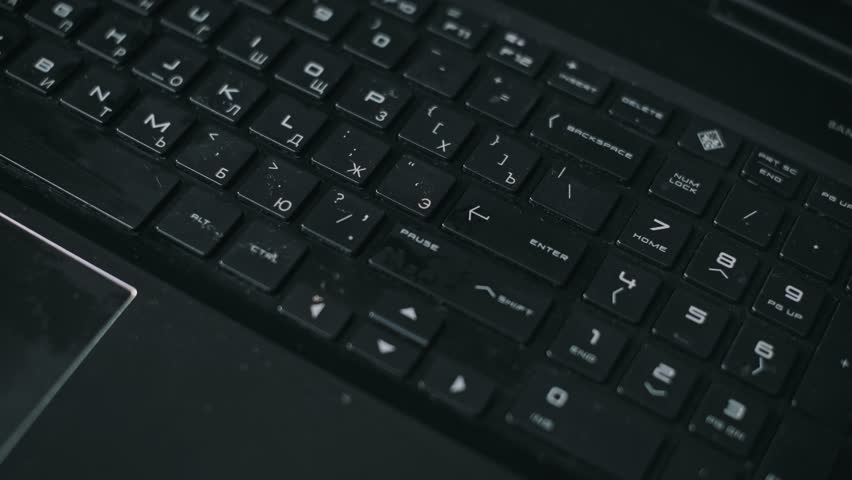 Closeup hand spraying antiseptic liquid from a white bottle onto a dusty black laptop keyboard, then wiping the keys clean with a white cotton pad. Disinfecting electronics for hygiene and prevention