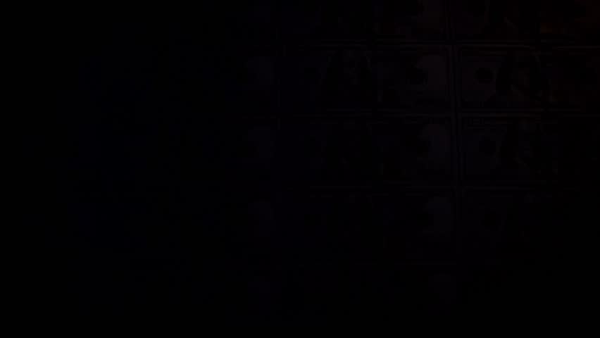 Top view of a hand using an ultraviolet lamp to check for counterfeit money, moving the UV beam over an uncut sheet of hundred dollar bills to reveal the glowing pink security thread on each banknote.