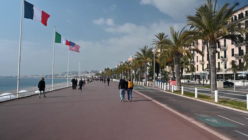 People walking along the Promenade des Anglais in Nice, France, on a sunny day, enjoying the seaside view and relaxed Mediterranean atmosphere.