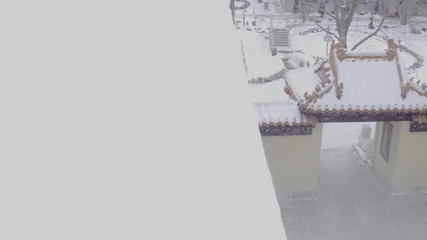 Drone view of snowy entrance gate to Chinese temple garden, D-Log footage