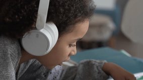 Primary school African American Student child with headphones hand writing in book using laptop. Distance learning online education. School girl studying at home with digital tablet computer and doing - Powered by Shutterstock - Get 15% off with code: PIKWIZARD15