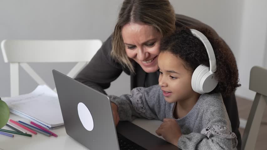 Caucasian mother and African American daughter studying at home, mom teaching math doing homework in cosy white room. Parent teach, child school girl learn mathematics, write exercise read book