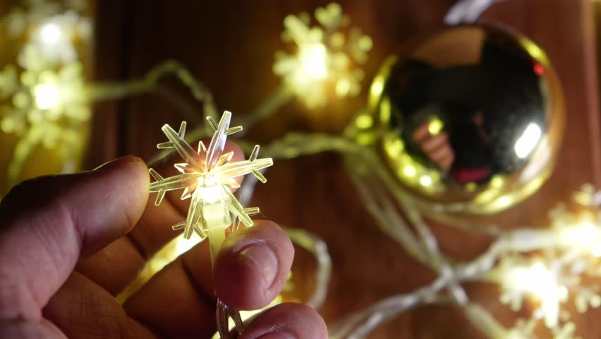 Hand holding glowing snowflake christmas light with golden ornaments in the background with copy space. - Powered by Shutterstock - Get 15% off with code: PIKWIZARD15