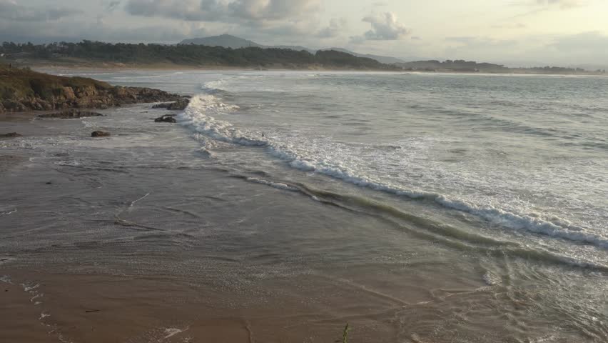 Panoramic view capturing the stunning coastline, where tranquil ocean waves caress the soft sandy beach. The rugged shore is adorned with rocks and lush vegetation, adding to its natural beauty